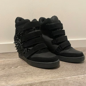 Svarta sneakers med nitar - Svarta sneakers med kilklack och nitar på sidorna. Skorna har kardborreband. Okänd storlek men passar inte mig (40/41) så skulle gissa på storlek 37,38 eller 39