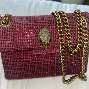 Röd glittrig axelväska från Kurt Geiger - Limited edition röd axelväska från Kurt Geiger med glittrigt rutigt mönster och guldfärgad kedja. Kensington modellen, mini. Använd men i fint skick, tappat några av de glittriga stenarna men ingenting märkbart.