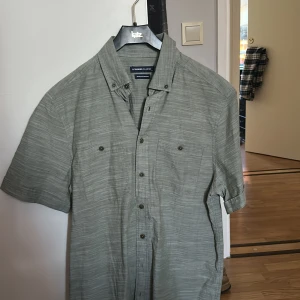 Grön kortärmad skjorta från LC Waikiki - Säljer en stilren grön kortärmad skjorta från LC Waikiki. Skjortan har en klassisk krage och knappar framtill. Perfekt för en avslappnad look.