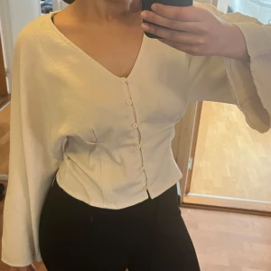 Vit blus med knappar - Creamfärgad blus med knappar framtill. Blusen har en v-ringad design och vida ärmar. 