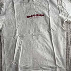 Vit t-shirt med tryck från Boohoo - Säljer en vit oversize t-shirt från Boohoo med tryck i rött och svart på bröstet. T-shirten har en klassisk rund hals och korta ärmar. Perfekt för en avslappnad stil.