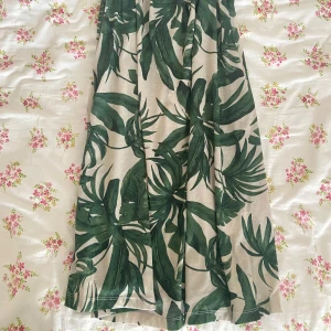 Grönmönstrad klänning med axelband - Somrig klänning med grönt bladmönster på en beige bakgrund. Klänningen har smala axelband och en luftig passform. Mjukt och bekvämt material.