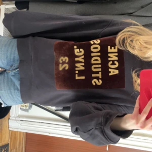 Svart sweatshirt från Acne Studios - Säljer en svart sweatshirt från Acne Studios med en stor brun och beige logga på framsidan. Tröjan har långa ärmar och en avslappnad passform. Perfekt för en casual look.