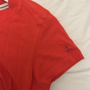 Röd t-shirt från Calvin Klein Jeans - Snygg röd t-shirt från Calvin Klein Jeans med korta ärmar . T-shirten är då lite söndrig nere vid botten då jag går sänka priset lite. När jag köpte tröjan kostade den runt 400-500kr men nu säljer jag för 199kr. Tröjan kan se orange ut i bilden men den är  röd. Pris kan diskuteras 