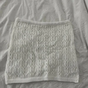 Vit stickad kjol - Säljer en söt vit stickad kjol med ett fint hålmönster. Kjolen är kort och har en elastisk midja för en bekväm passform. har aldrig använts, i storlek S 