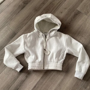 Lounge Grå croppad hoodie - Säljer en stilren grå croppad hoodie från Lounge wear. Den har en dragkedja framtill och en bekväm huva. Perfekt för en avslappnad look. Nypris 799:-