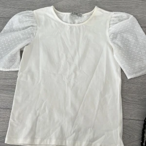 Vit topp med puffärmar från Stradivarius - Säljer en stilren vit topp från Stradivarius med unika puffärmar i ett prickigt mönster. Toppen har en rund halsringning och är perfekt för en trendig look. Passar bra till både jeans och kjol.