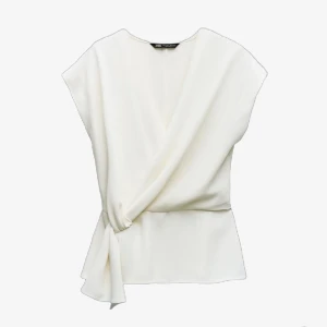 Vit topp från Zara - Säljer en stilren vit omlottopp från Zara. Toppen har en elegant v-ringning och knytning i sidan som ger en fin siluett. Perfekt för en chic och modern look.