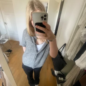 Grå kofta med knappar - Säljer en grå kofta med korta ärmar och knappar framtill. Perfekt för lager-på-lager och passar till många olika outfits. Enkelt och snyggt val för både vardag och lite finare tillfällen.