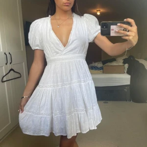 Vit klänning med puffärmar -  vit klänning med v-ringning och puffiga kortärmar. Klänningen har volanger och spetsdetaljer perfekt för sommaren 