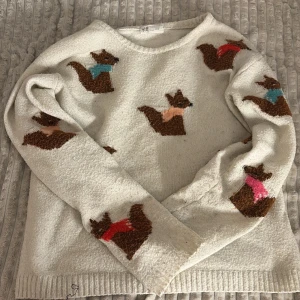 Cream tröja med jätte gulliga ekorrar  - Mysig vit tröja från H&M med bruna ekorrar i färgglada tröjor. Perfekt för en avslappnad stil med en lekfull touch. Tröjan har långa ärmar och ribbade kanter.