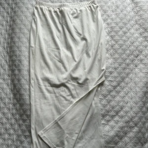 Vit lång kjol - Säljer en vit lång kjol med diskret randigt mönster. Byxorna har en elastisk midja för extra komfort och är tillverkade i ett mjukt material. Perfekta för en avslappnad stil. Dubbel tyg halvvägs som kan synas i ljuset men annars superfin. Det är en slit på sidan av kjolen🦋 helt oanvänd