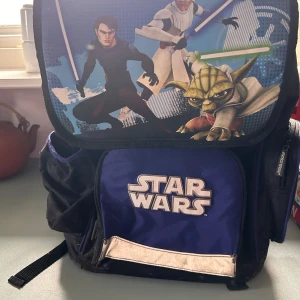 Star Wars ryggsäck - Cool Star Wars ryggsäck med motiv av kända karaktärer och logotyp. Ryggsäcken är svart och blå med flera fack och justerbara axelremmar. Oskrivet schema på insidan av locket. Perfekt för skolan eller utflykter för alla Star Wars-fans.