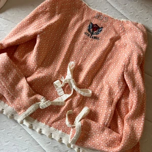 Orange kofta från Odd Molly - Säljer en söt orange kofta från Odd Molly med ett broderat motiv och texten 'Rise Above'. Koftan har knytband framtill och vita detaljer vid ärmslut och nederkant. Perfekt för en avslappnad stil med en touch av unik design. 🌸