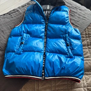 Replay väst ljusblå - Snygg blå dunväst från Replay med dragkedja och ribbade kanter. Perfekt för kyligare dagar. Västen är i knappt använt skick. Passform: 155-165cm.