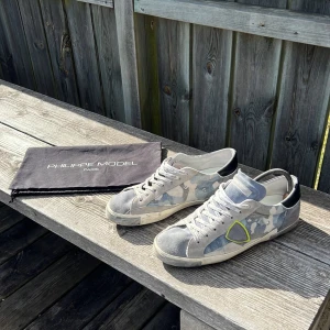 Camouflage sneakers från Philippe Model - Snygga sneakers från Philippe Model i en cool grå och blå camouflage-design. Skorna har snörning och en kontrasterande svart häl. Perfekta för en stilren och avslappnad look. Dustbagen inngår! Passar till dig som har 42-43. Skicket är 8/10, använda några få gånger. Hör av dig vid minsta fråga👍🏼 (kan också tänka mig byta mot några andra skor i stl 44) väldigt sällsynta då de är de ända på plick.