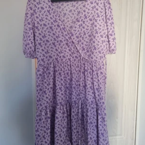 Lila blommig klänning GinaTricot - Kort blommig klänning från GinaTricot. Endast använd en handfull gånger. Volanger i kjolen och band för att knyta i midjan. Stretchig i midjan.