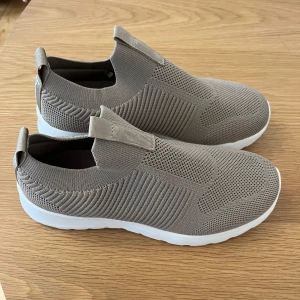 Beige stickade sneakers från Beez - Snygga och bekväma beige sneakers från Beez med stickad ovandel och elastisk passform. Skorna har en vit sula med bra grepp och är perfekta för en avslappnad stil. Lätta att ta på och av tack vare den elastiska designen.