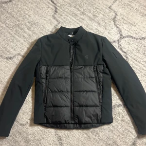 Svart cardigan från Calvin Klein - Snygg svart cardigan från Calvin Klein  med quiltad design på framsidan. Jackan har dragkedjor och en stilren look, perfekt för både höst och vår. Den är långärmad och har en modern passform. Helt nytt !! Storlek M men kan passa S