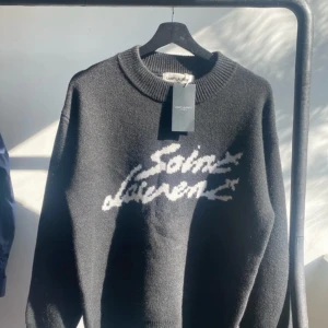 Svart tröja från Saint Laurent - Snygg svart tröja från Saint Laurent med vit logotyp på framsidan. Tröjan har en klassisk rund hals och långa ärmar, perfekt för en stilren look. Tillverkad i Italien.