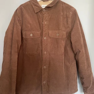 Brun manchesterjacka från Kappahl - Säljer en snygg brun manchesterjacka från Kappahl. Jackan har långa ärmar och knappar framtill samt två bröstfickor med knappar. Perfekt för en stilren look!