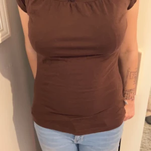 Brun kortärmad topp - Säljer en brun kortärmad topp med rund halsringning. Toppen har en tight passform och är perfekt för en avslappnad stil. Den är gjord i ett mjukt och bekvämt material.