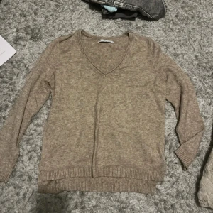 Beige stickad tröja från ONLY - Säljer en mysig beige stickad tröja från ONLY med v-ringning. Tröjan har långa ärmar och ribbstickade muddar vid ärmslut och nederkant. Perfekt för kyliga dagar!