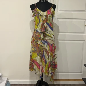 Asymmetrisk meshklänning - Säljer en superhärlig klänning med färgstarkt abstrakt mönster i gult, rosa, blått och grönt. Klänningen har smala axelband, volangdetaljer framtill och asymmetrisk nederkant. 