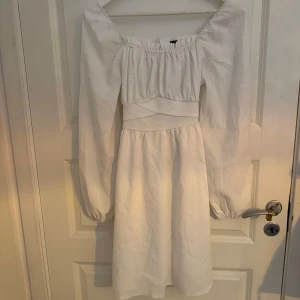 Vit kortklänning med puffärmar från SHEIN - Superfin vit kortklänning från SHEIN med långa puffärmar och markerad midja. Klänningen har en snygg omlottkänsla baktill med knytband och resår vid axlarna. Perfekt för dig som gillar romantisk och trendig stil.