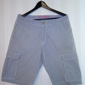 Randiga cargoshorts från Etirel - Snygga cargoshorts från Etirel i blåvitt randigt mönster. De har flera praktiska fickor på sidorna och klassisk dragkedja framtill. Tillverkade i 100% bomull för en skön känsla, perfekta för varma dagar. Passar dig som gillar avslappnad och sportig stil.                               Kan skickas med extra pris via post.              