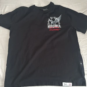 Svart Hoodrich t-shirt med tryck - Svart t-shirt från Hoodrich i storlek L med stort grafiskt tryck på ryggen och mindre tryck på bröstet. Trycket har motiv av en bevingad häst och texten 'Product Of The Streets'. T-shirten har rund hals och är kortärmad, tillverkad i mjuk bomull.