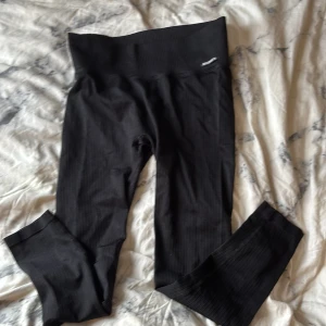 Svarta ribbade leggings från MM Sports - Svarta leggings från MM Sports i ribbat material med hög midja. Snygg och bekväm passform som sitter tight och följer kroppen. Perfekta för gymmet eller chill hemma. Diskret logga på höften och stretchigt tyg som ger bra rörelsefrihet.