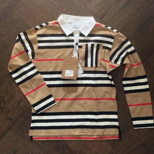 Burberry pikétröja - Säljer en helt ny pikétröja från Burberry som är aldrig använd eftersom jag inte gillade den. Originalproset på tröjan är 1649 kr. Tröjan är i size 12Y (152 cm). Pris kan diskuteras och skriv om fler bilder behövs. 