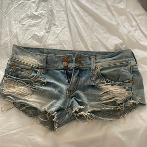 Rippade jeansshorts med fransar - Snygga ljusblå jeansshorts med slitna detaljer och fransig kant. Shortsen har låg midja, klassiska fickor fram och bak samt dubbla knappar i gylfen. Perfekta för sommaren och ger en cool, avslappnad vibe.