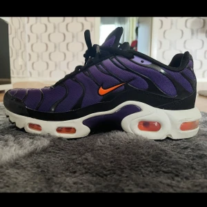 Nike Air Max Plus lila och svart - Nike Air Max Plus sneakers i lila mesh med svarta detaljer och orange swoosh. Skorna har vit sula med synliga Air Max-enheter och svarta snören. Tn-logga bak och cool vågig design på ovandelen. Priset går även att diskutera