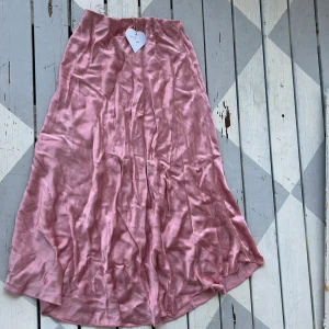 Ljusrosa långkjol i satin - Supersnygg ljusrosa långkjol i glansigt satinmaterial. Helt oanvänd med prislapp kvar! 