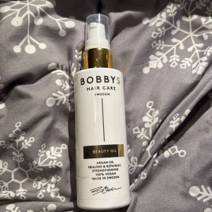 Bobbys Beauty Oil Arganolja - Bobbys Beauty Oil är en arganolja för håret som stärker, reparerar och ger glans. 100% vegansk och tillverkad i Sverige. Kommer i en vit plastflaska med gulddetaljer och pumpfunktion för enkel applicering.