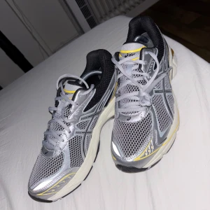 Asics GEL-1130 silver/gul sneakers - Snygga Asics GEL-1130 sneakers i silver, svart och gult med mesh-överdel och klassiska Asics-detaljer. Skorna har en chunky sula, snörning och reflekterande inslag. Perfekta för dig som gillar retrovibbar och sportig stil. Storlek 42,5. Passar även 41. Aldrig använt. Nypris 1700 kr.