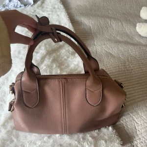 Rosa Brun väska - Jättefin rosa brun handväska i typ skinnmaterial. Jättepraktisk då den är rymlig och har flera fack. Perfekt till skolan eller till vardags. Den är i bra kvalitet då den knappt är använd