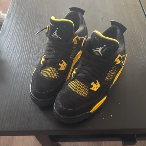Nike Jordan 4 svart/gul sneakers - Säljer ett par Nike Air Jordan 4 sneakers i svart och gul med coola meshdetaljer och Jumpman-logga på plösen och sulan. Skorna har snörning, platt sula och en snygg kontrast mellan svart mocka och gula inslag. Perfekt för dig som vill sticka ut med din stil.