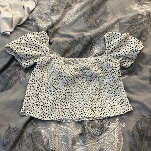 Prickig blus med puffärm från Stradivarius - Supersöt vit blus med svarta prickar från Stradivarius. Modellen är croppad med smockad kropp och puffiga korta ärmar. Tyget är lätt och stretchigt, perfekt för en trendig look. Säljer då den inte kommer till användning längre!