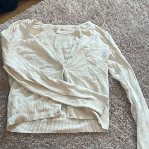 Vit kofta från H&M Basics XXS - En stilren vit kofta från H&M Basics i storlek XXS. Koftan har v-ringning, långa ärmar och knappar framtill. Tillverkad i mjukt bomullsmaterial med ribbade muddar vid ärmslut och nederkant. Perfekt för lager-på-lager och enkel att matcha.