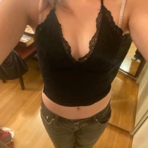 Svart spetsig croppad halterneck festtopp - Svart croppad halterneck topp med snygga spetsdetaljer och djup v-ringning. Perfekt festtopp! Toppen har knyt i nacken och är ärmlös, vilket ger en öppen rygg.