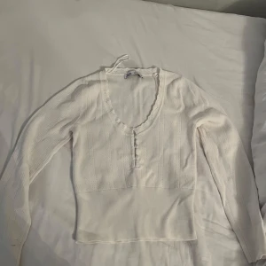Vit stickad topp med knappar från Zara - Supersöt vit pointelle stickad topp från Zara med lång ärm, v-ringning och dekorativa knappar framtill. 