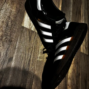 Adidas Spezial svarta sneakers mocka - Svarta Adidas Spezial sneakers i mocka med klassiska vita ränder på sidorna och detaljer i vitt. Snygg retrostil med svart sula och guldfärgad Spezial-logga. Skorna har snörning och rund tå, perfekt för dig som gillar streetwear dessa skor är använda inomhus 3 gånger. Storlek 46 jag är st 45 om dom sitter bra.