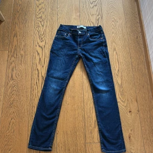 Levi's 512 Slim Taper jeans blå - Snygga Levi's 512 Slim Taper jeans i mörkblå denim. Modellen har smal passform med avsmalnande ben, klassiska fem fickor och orangea sömmar. Perfekta för dig som gillar en modern och stilren look.