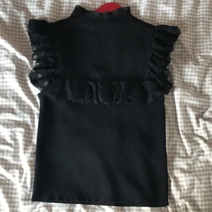 Svart volangtopp från Zara - Supersnygg svart topp från Zara. Sitter tajt mot kroppen och ger en väldigt classy look. Tyget uppe är lite genomskinligt men eftersom det är svart tyg så inte för genomskinlig, perfekt! Storlek S💕 skriv för frågor