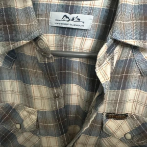 Rutig skjorta från Hysteric Glamour - Snygg rutig skjorta från Hysteric Glamour i beige och blått. Skjortan har klassisk krage, två bröstfickor med knappar och långa ärmar. Riktigt kylig och väldigt bra skick. Storlek S