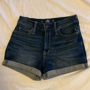 Mörkblå jeansshorts från Hollister - Har tyvärr vuxit ur dessa fina och bekväma mörkblå jeansshorts från Hollister, som har en klassisk femficksdesign och uppvikta nertill. Shortsen är väldigt stretchiga och är högmidjade med en liten Hollister-logga på bakfickan. Perfekta för varma dagar och enkel att matcha med din favorit-topp💙
