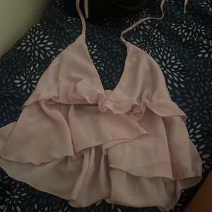 Ljusrosa volangig linnetopp knyt - Supersöt ljusrosa linnetopp med volanger och tunna knytband i nacken. Toppen har en flowy och luftig känsla, perfekt för varma dagar eller när du vill känna dig extra feminin. Djup v-ringning och omlottkänsla framtill.